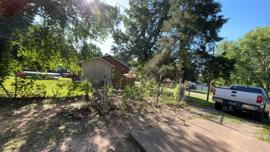 A pickup truck is parked near a house surrounded by trees and a sunny yard. A playground is visible in the background.